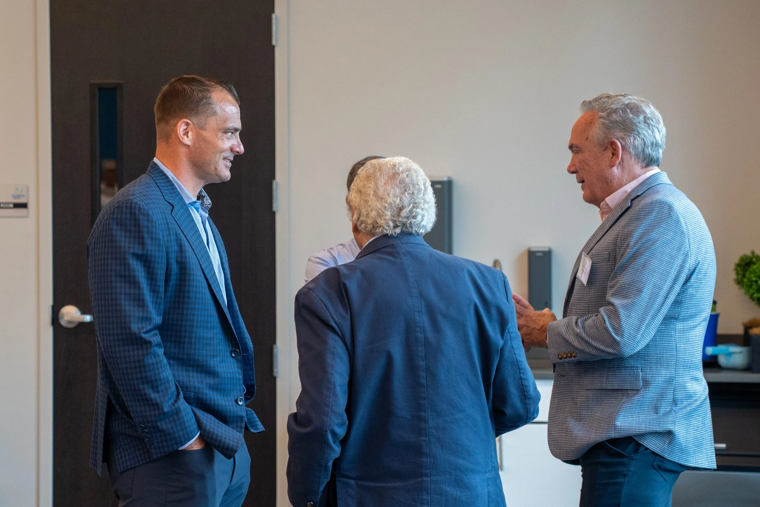 Three men in business attire talk together at a networking event in an office