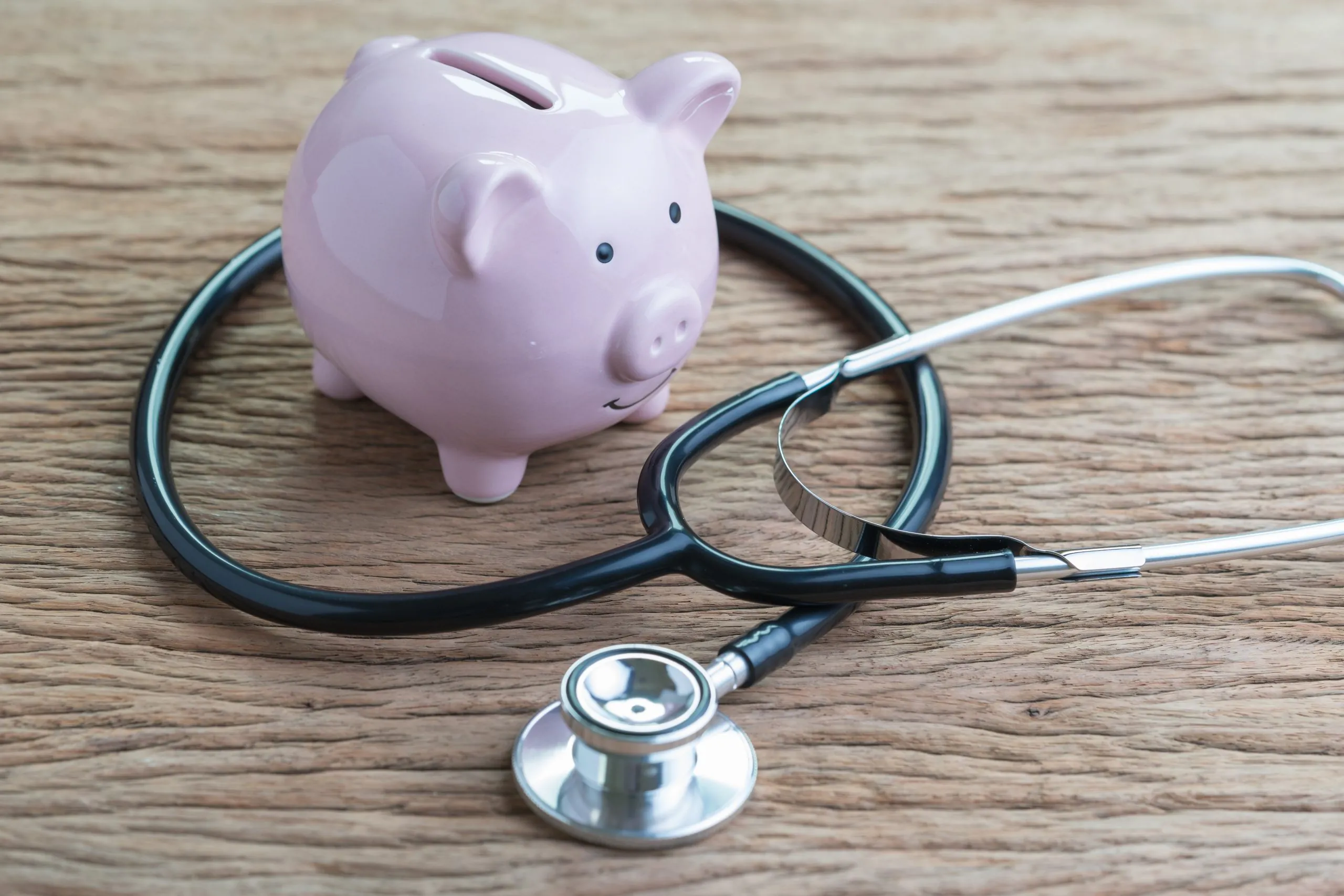 Pink piggy bank beside a black stethoscope on a wooden surface