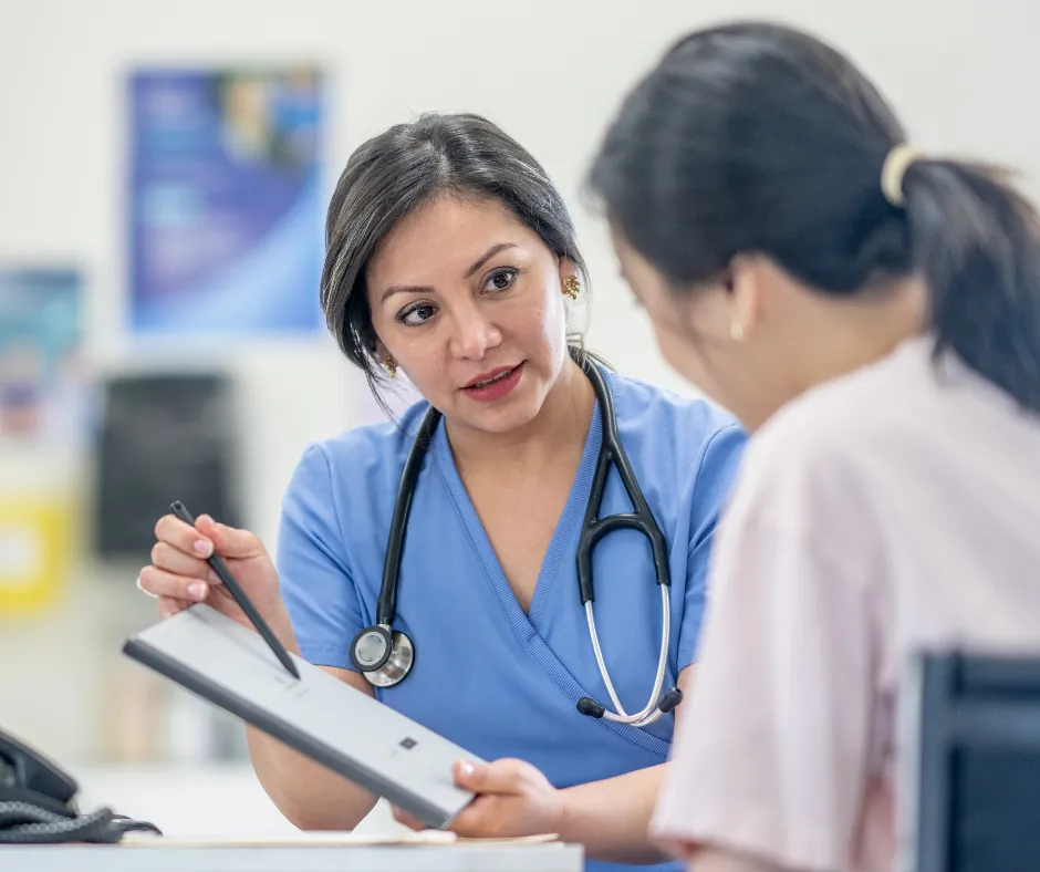 Healthcare worker in blue scrubs with a stethoscope reviews a tablet with a patient